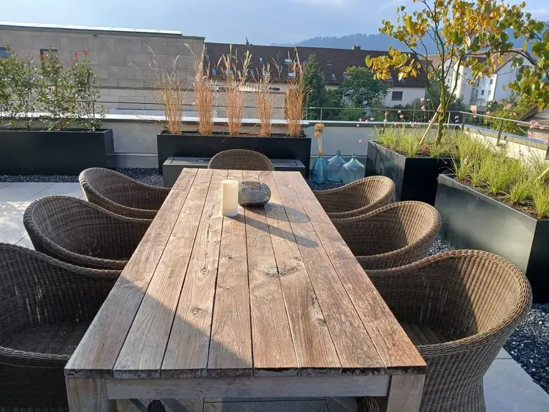 Gartentisch mit Rattanstühlen auf begrünter Dachterrasse