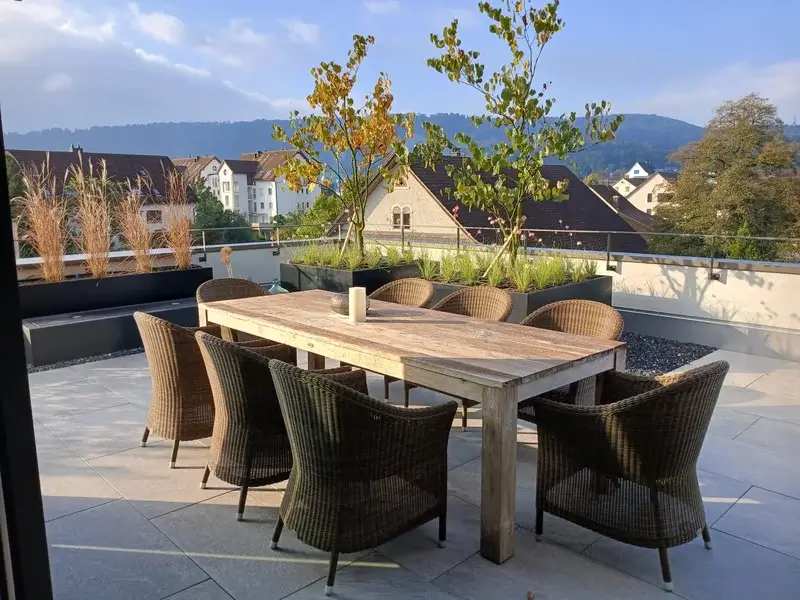 Gesamtansicht einer bepflanzten Dachterrasse mit Holz-Esstisch