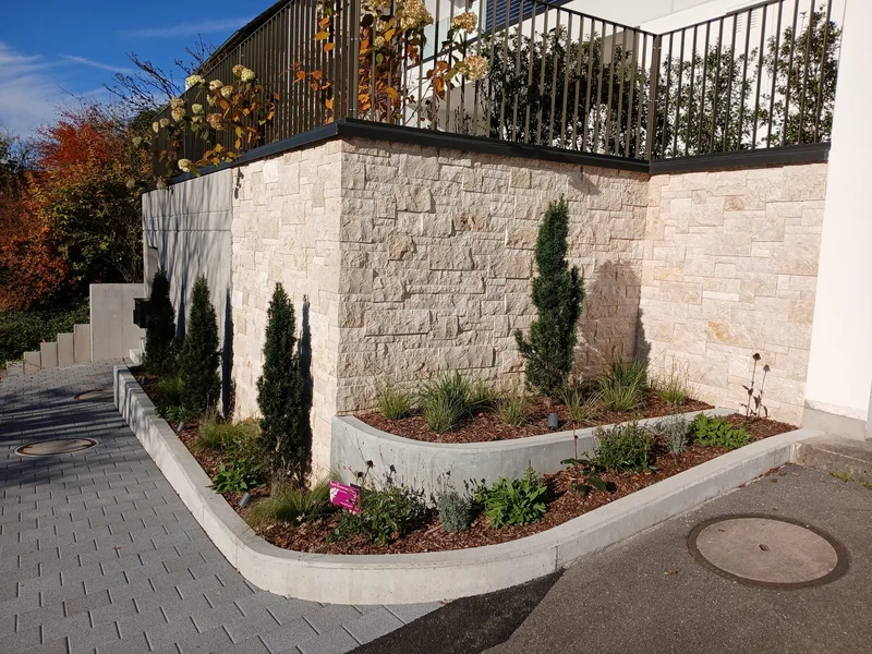 Verblendete Betonmauer mit Naturstein und frischer Bepflanzung